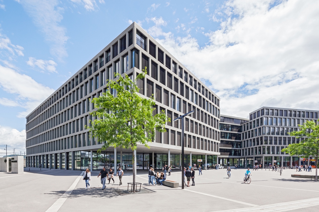  Sur la photo, on voit le campus de Brugg-Windisch. 
Il y a plusieurs bâtiments.
Les bâtiments sont modernes.
Il y a des gens sur la place devant le campus. 